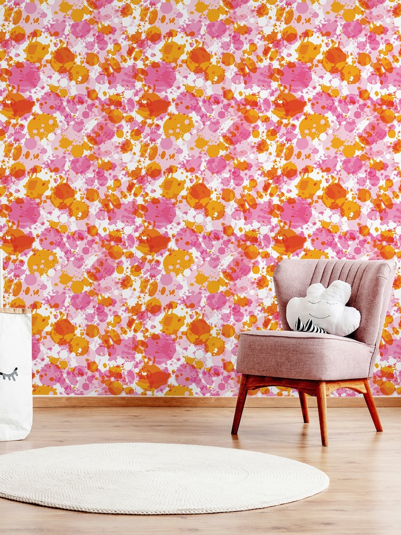 May include: A pink and orange splatter paint pattern wallpaper with a pink chair and a white rug in front of it.