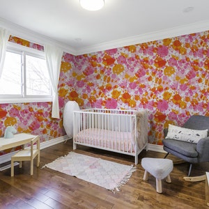 May include: A nursery room with a white crib, a rocking chair, a small table and chairs, and a rug. The walls are covered in a pink and orange splatter paint wallpaper.