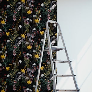 May include: A roll of black and white floral wallpaper with a ladder leaning against a white wall. The wallpaper features a variety of flowers and leaves in a repeating pattern.