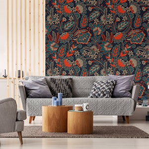 May include: A gray sofa with pillows sits in front of a wall with a teal, orange, and brown floral wallpaper pattern. Two wooden side tables with a cup on one of them are in front of the sofa.
