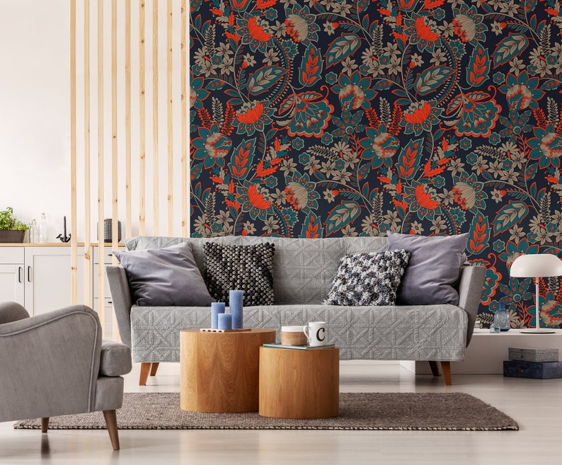 May include: A gray sofa with pillows sits in front of a wall with a teal, orange, and brown floral wallpaper pattern. Two wooden side tables with a cup on one of them are in front of the sofa.