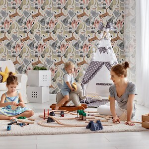 May include: A playroom with a white armchair, a teepee tent, and a wooden toy train set. Two children are playing with the train set, while a woman sits on the floor and watches them. The walls are covered in a colorful wallpaper with a pattern of animals.
