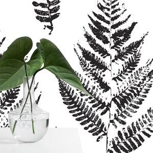 K&ouml;nnte beinhalten: Eine klare Glasvase mit einer breiten &Ouml;ffnung und einem runden K&ouml;rper, gef&uuml;llt mit Wasser und zwei gr&uuml;nen Bl&auml;ttern. Die Vase steht auf einer wei&szlig;en Oberfl&auml;che vor einer schwarz-wei&szlig;en Tapetenmuster mit Farn.