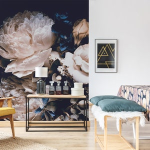 K&ouml;nnte beinhalten: Eine florale Tapeten-Wandmalerei mit gro&szlig;en wei&szlig;en Pfingstrosen und blauen Blumen auf einem dunklen Hintergrund. Die Wandmalerei ist in einem Wohnzimmer mit einem gelben Sessel, einem Holz-Konsolentisch und einer schwarzen Pendelleuchte dargestellt.