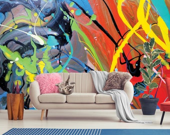 Könnte beinhalten: Ein Wohnzimmer mit einem hellbeigen Sofa, einem rosa Kissen, einer grauen Wolldecke, einer Topfpflanze und einem Holz-Beistelltisch. Die Wand hinter dem Sofa ist mit einem farbenfrohen abstrakten Gemälde bedeckt, das Spritzer in Blau, Grün, Gelb, Rot und Schwarz zeigt.