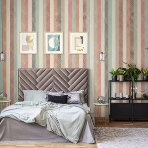 Puede incluir: Un dormitorio con una cama tapizada en gris con un cabecero de patr&oacute;n de chevron. Las paredes est&aacute;n cubiertas con un papel tapiz a rayas con un patr&oacute;n de espiga. Hay tres impresiones de arte abstracto enmarcadas en la pared sobre el cabecero. Hay una estanter&iacute;a de metal negro con plantas y art&iacute;culos decorativos.