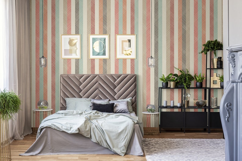 Puede incluir: Un dormitorio con una cama tapizada en gris con un cabecero de patr&oacute;n de chevron. Las paredes est&aacute;n cubiertas con un papel tapiz a rayas con un patr&oacute;n de espiga. Hay tres impresiones de arte abstracto enmarcadas en la pared sobre el cabecero. Hay una estanter&iacute;a de metal negro con plantas y art&iacute;culos decorativos.