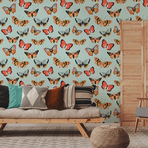 May include: A light blue wall with a repeating pattern of colorful butterflies. The butterflies are in various shades of orange, yellow, red, and black. The wall is decorated with a wooden slatted screen, a couch with pillows, and a chair.