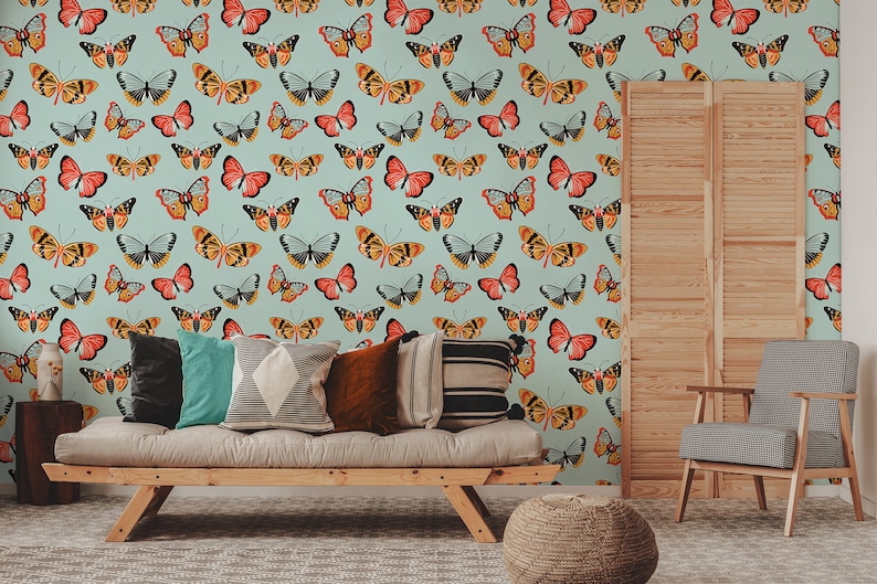 May include: A light blue wall with a repeating pattern of colorful butterflies. The butterflies are in various shades of orange, yellow, red, and black. The wall is decorated with a wooden slatted screen, a couch with pillows, and a chair.