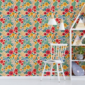 May include: A white bookshelf with three shelves, decorated with wooden geometric shapes and potted plants, against a wall covered in a floral wallpaper with red, yellow, and blue flowers on a cream background.