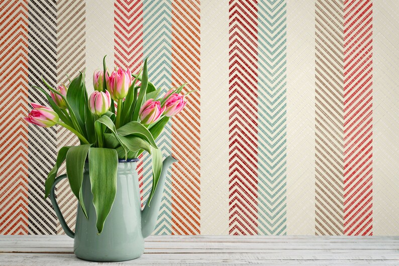 Puede incluir: Un ramo de tulipanes rosas en una jarra de esmalte azul claro sobre un fondo de rayas de chevron rojas, azules y marrones.