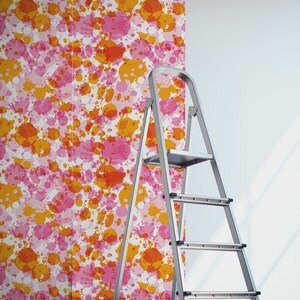 May include: A roll of wallpaper with a pink and orange splatter paint design. A silver step ladder is in the foreground.
