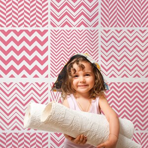 Puede incluir: Una niña pequeña con un sombrero hecho de una revista sostiene dos rollos de papel tapiz blanco frente a una pared con un patrón de chevron rosa y blanco.