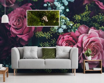 May include: A close-up of a floral arrangement featuring pink roses and greenery. The roses are in full bloom and have a velvety texture. The greenery is a mix of ferns and other leafy plants. The arrangement is set against a dark background.