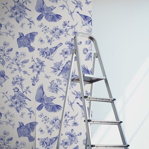 May include: A white wallpaper with a blue floral pattern featuring birds and flowers. The wallpaper is being installed on a wall with a ladder nearby.