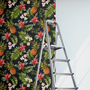 May include: A roll of tropical-themed wallpaper with pineapples, flowers, and leaves on a black background. A silver ladder is leaning against a wall with the wallpaper partially applied.