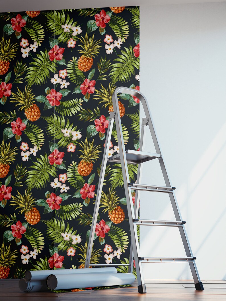 May include: A roll of tropical-themed wallpaper with pineapples, flowers, and leaves on a black background. A silver ladder is leaning against a wall with the wallpaper partially applied.