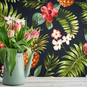 May include: A bouquet of pink tulips in a blue enamel pitcher against a backdrop of a dark blue floral wallpaper featuring tropical leaves, pineapples, and hibiscus flowers.