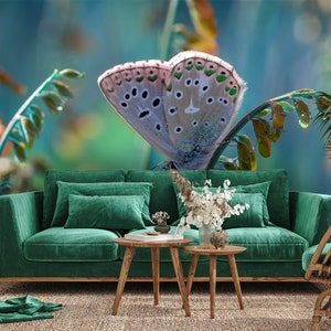 May include: A close-up of a butterfly with light blue wings and dark spots, perched on a green plant. The butterfly is set against a blurred background of green and blue hues. A green velvet sofa and wooden tables are in the foreground.