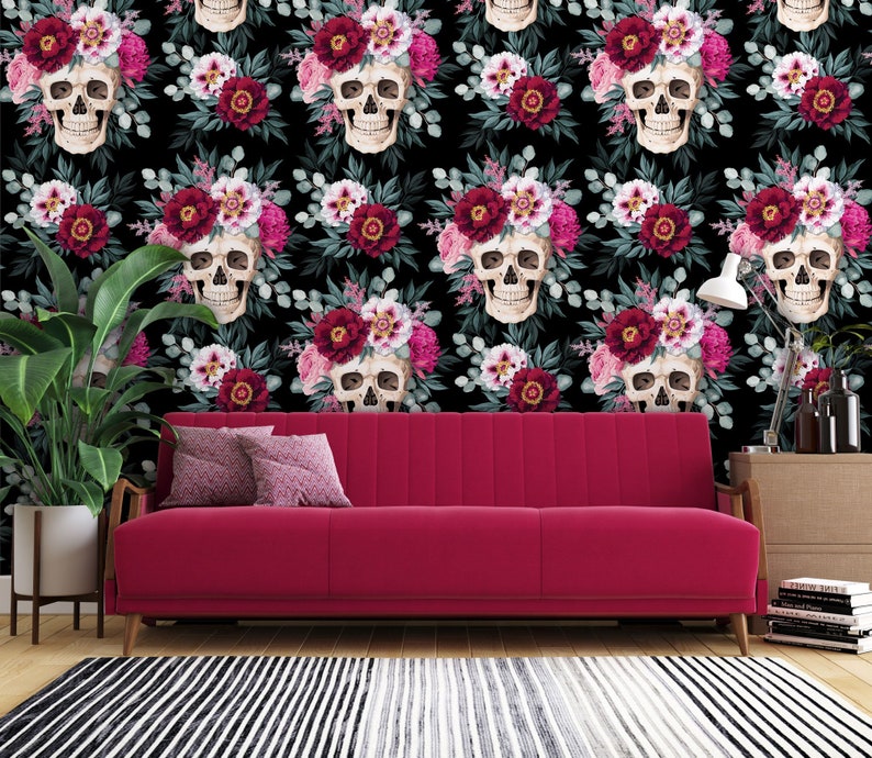 May include: A black background with a repeating pattern of white skulls wearing floral crowns of pink and burgundy flowers. The skulls are surrounded by green leaves. A red sofa sits in front of the wallpaper.