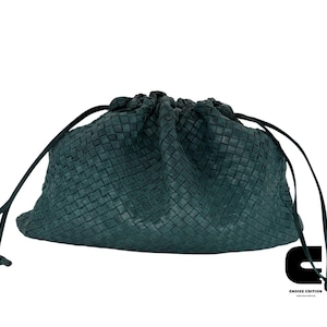 May include: A teal green woven drawstring bag with a knotted closure. The bag has a textured appearance and a dark cord for cinching. The bag is set against a white background.
