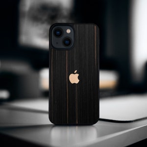 Puede incluir: Una funda negra para iPhone con un patrón de veta de madera y un logotipo de Apple dorado.