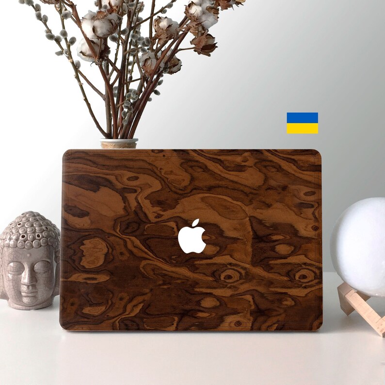 May include: A laptop computer with a wood grain design on the cover. The Apple logo is visible on the cover. The laptop is sitting on a white surface.