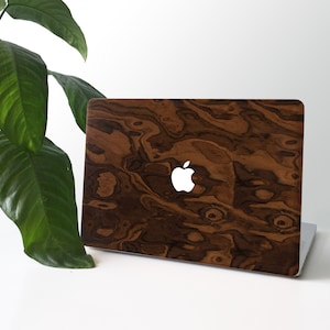 May include: A laptop computer with a wood grain design skin. The skin has a dark brown color with lighter brown swirls. The Apple logo is visible on the back of the laptop.