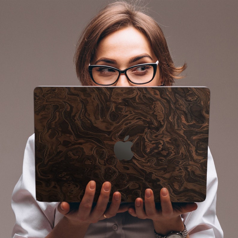 May include: A woman is holding a laptop computer with a brown wood grain design. The laptop has a silver Apple logo on the lid.