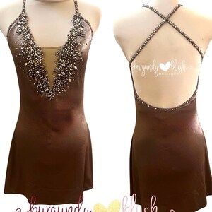 May include: A brown figure skating dress with a halter neckline and open back. The bodice is embellished with sparkling crystals and rhinestones. The dress has a short skirt and is displayed on a mannequin. The text "burgundy blush" is visible.