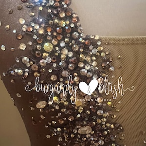 May include: Close-up of a brown garment embellished with shimmering rhinestones in gold, bronze, and clear hues. The text "burgandy & blush DESIGN STUDIO" is visible. The garment appears to be a formal dress or top.