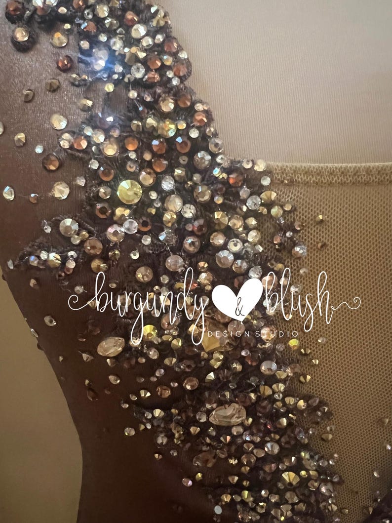 May include: Close-up of a brown garment embellished with shimmering rhinestones in gold, bronze, and clear hues. The text "burgandy & blush DESIGN STUDIO" is visible. The garment appears to be a formal dress or top.