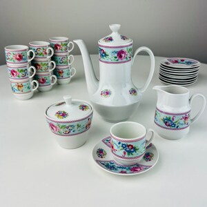 May include: A white porcelain tea set with a floral pattern in shades of pink, blue, and green. The set includes a teapot, creamer, sugar bowl, six cups, and six saucers.