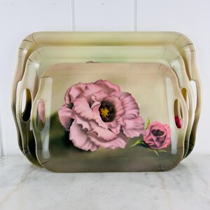 Pode incluir: Um conjunto de três bandejas encaixáveis com um design floral. As bandejas são feitas de um material de cor clara e apresentam uma grande rosa rosa com um centro amarelo e uma rosa rosa menor. O fundo é de cor verde claro.
