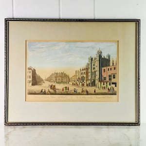 May include: An antique print of a street scene in London, England. The print shows a view of St. James's Palace and the Mall. The print is framed in a brown wood frame.