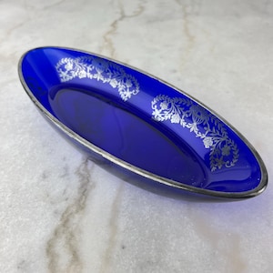 Può includere: Un piatto ovale blu cobalto con un motivo floreale argentato attorno al bordo.