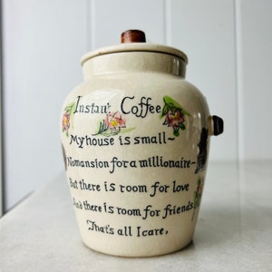 K&ouml;nnte beinhalten: Eine wei&szlig;e Kaffeedose aus Keramik mit einem Holzdeckel und handbemaltem Design. Die Dose tr&auml;gt ein Zitat, das lautet: "Instan: Coffee Myhouse is small- Nomansion for a millionaire- But there is room for love And there is room for friends. That's all Icare."