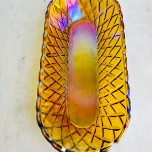 Pu&ograve; includere: Un piatto vintage in vetro ambrato con un motivo intrecciato. Il piatto ha una finitura iridescente ed &egrave; di forma ovale.
