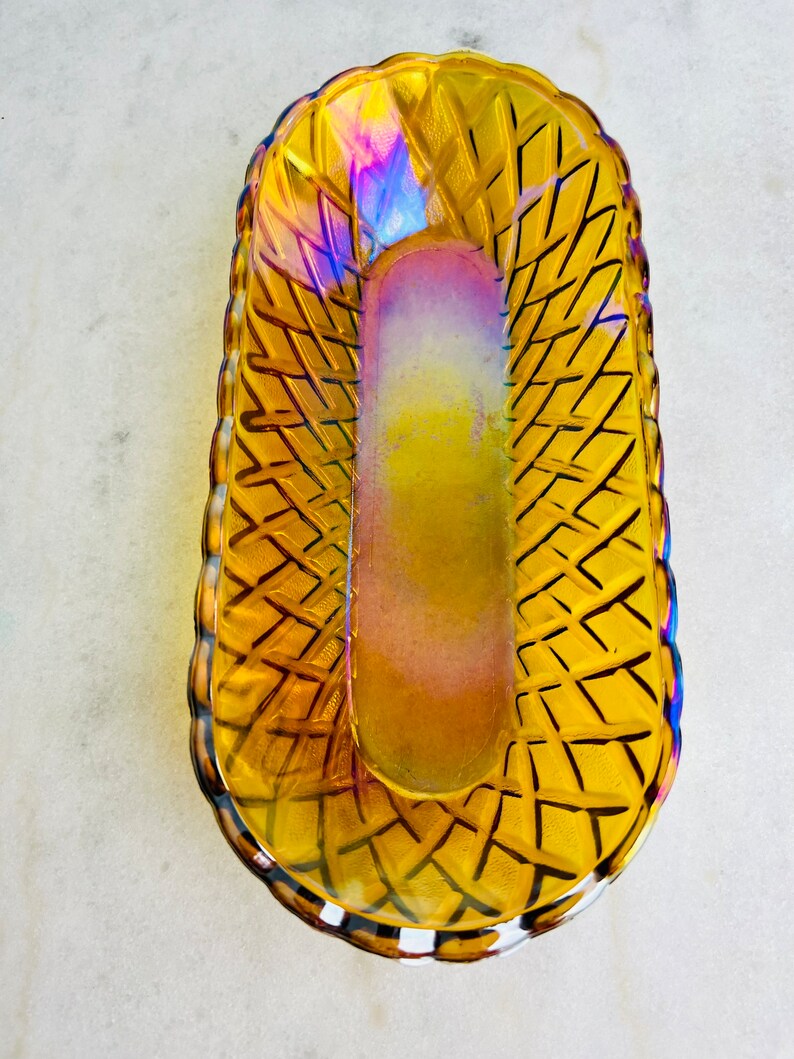 Pu&ograve; includere: Un piatto vintage in vetro ambrato con un motivo intrecciato. Il piatto ha una finitura iridescente ed &egrave; di forma ovale.