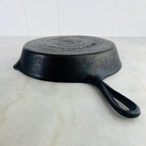 May include: Black cast iron skillet with a single handle. The skillet has a circular cooking surface and a slightly raised edge. The brand name "BROCKVILLE" is embossed on the bottom of the pan. The handle has a loop for hanging.