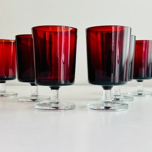 Può includere: Sei calici da vino rosso rubino, con steli e basi trasparenti, disposti su una superficie bianca. I calici hanno una forma cilindrica con un bordo leggermente svasato. Il colore dei calici è un rosso intenso.