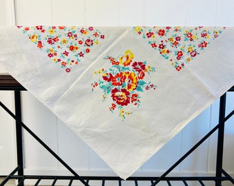 May include: White tablecloth with a floral pattern in shades of red, yellow, and blue. The tablecloth has a large floral bouquet in the center and smaller floral designs in the corners.