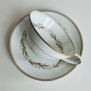 May include: A white teacup and saucer with a gold rim and a delicate floral design in gold.