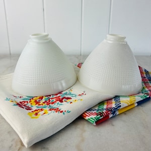 May include: Two white glass lampshades with a textured pattern. The lampshades are sitting on a colourful fabric.