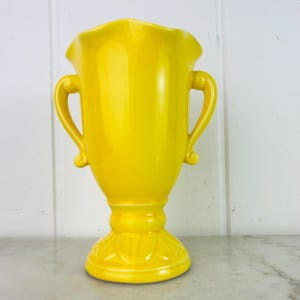 Peut inclure: Un vase en céramique jaune vif avec deux anses. Le vase a un design classique et traditionnel avec une base cannelée.