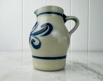 May include: A gray stoneware pitcher with a blue and white floral design. The pitcher has a handle and a spout.