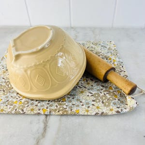 Peut inclure: Un saladier en céramique beige avec un motif de losanges décoratifs et un rouleau à pâtisserie en bois reposent sur un tissu à motifs floraux. Le rouleau à pâtisserie mesure environ 30 cm de long.