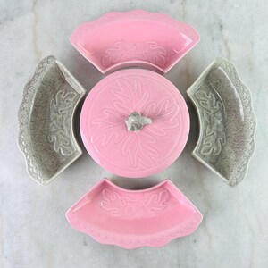 Puede incluir: Una fuente de cerámica rosa con tapa y tres platos en forma de abanico. La tapa y los platos en forma de abanico tienen un diseño floral. Los platos en forma de abanico son grises y rosas. La fuente tiene un pomo gris.