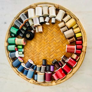 Pode incluir: Uma cesta de vime cheia de carretéis de fio de várias cores, incluindo vermelho, verde, azul e branco.