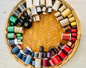 Può includere: Un cesto di vimini pieno di bobine di filo di vari colori, tra cui rosso, verde, blu e bianco.